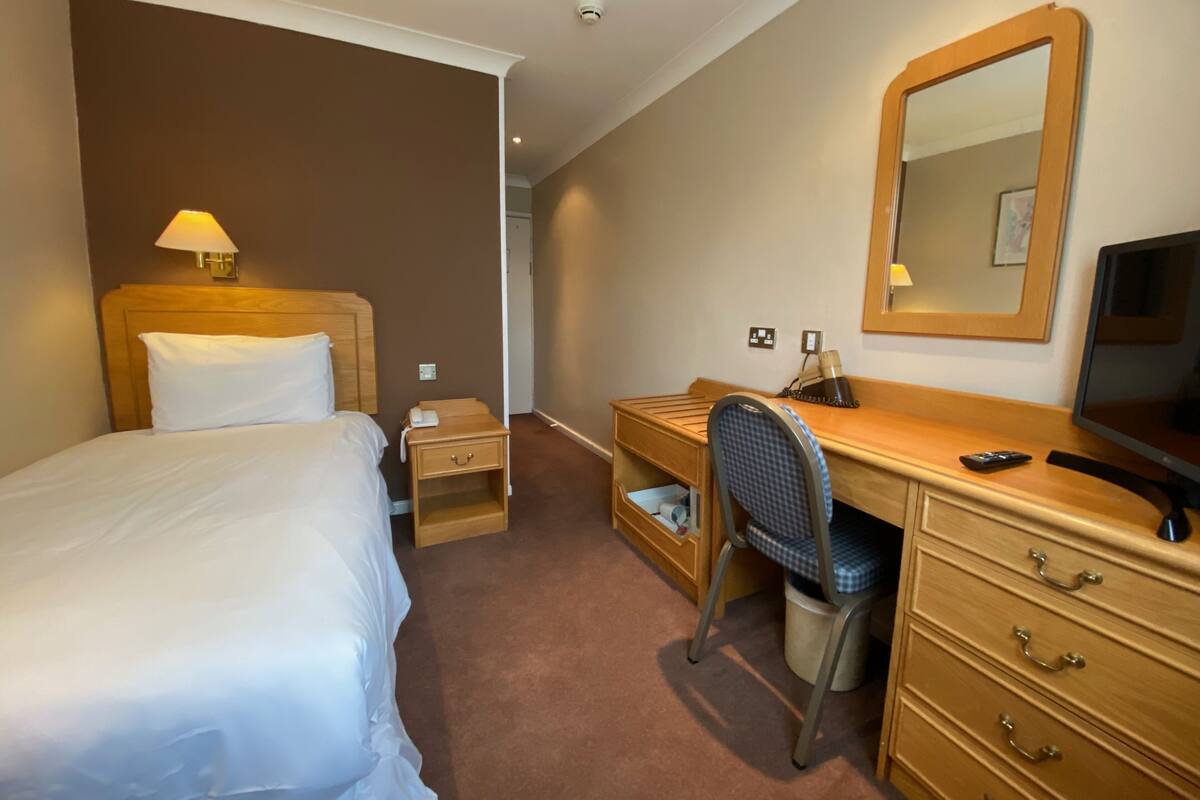 A hotel room with a bed, a desk, a chair, a dresser, a mirror, and a television.