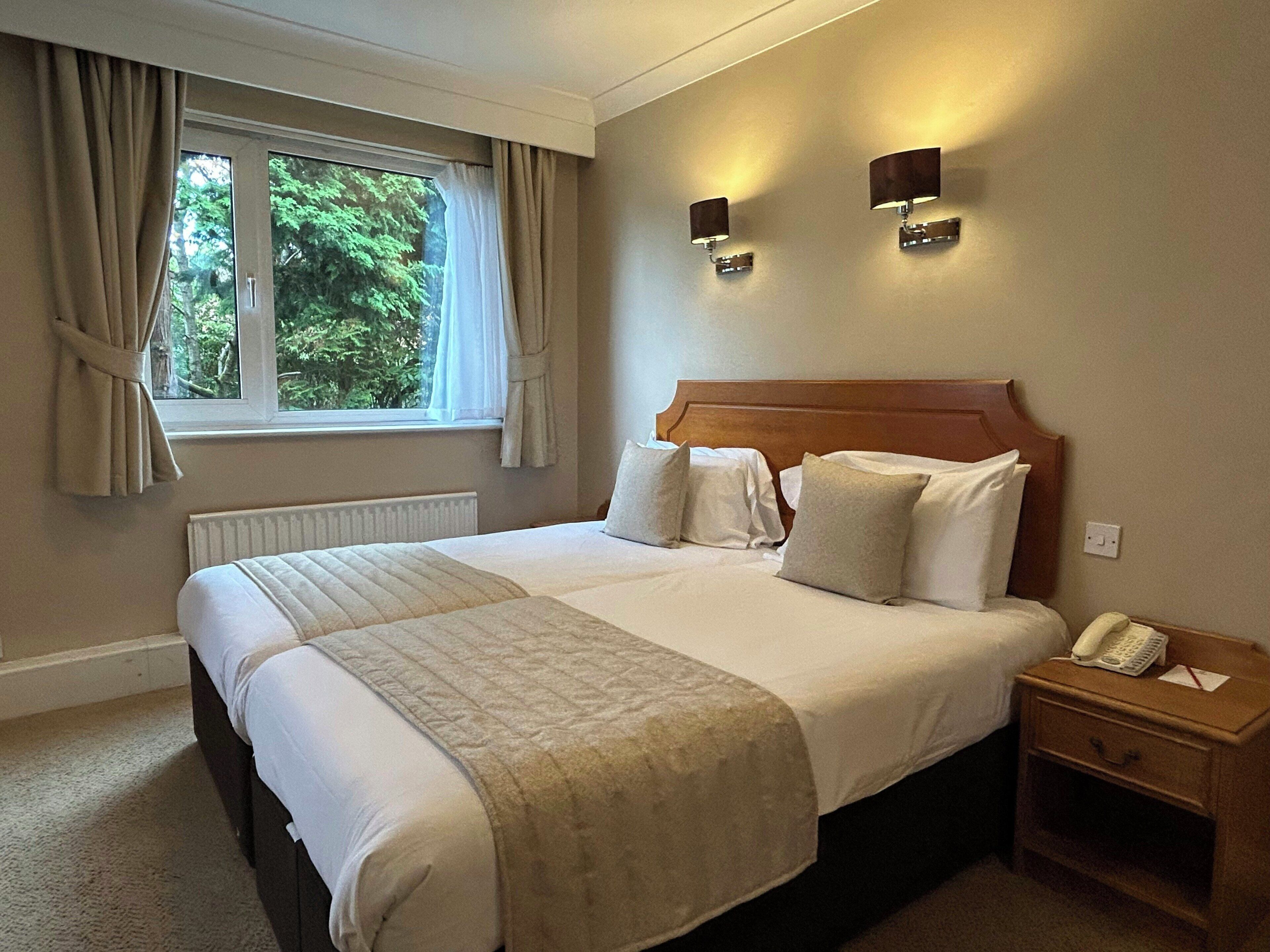 Una habitación de hotel con una cama grande, una mesita de noche con teléfono y una ventana con cortinas.