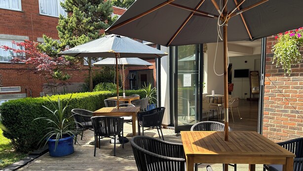 An outdoor patio area with wooden tables and chairs, umbrellas, and potted plants. - The Great Barr Hotel (Birmingham)
