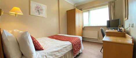 A hotel room with a bed, bedside table, lamp, desk, chair, television, and a window with curtains.