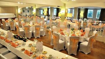 A banquet hall with round tables set for a formal event, featuring white tablecloths and orange sashes on chairs.