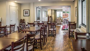A spacious dining area with multiple wooden tables and chairs, a large window with curtains, and a banner with a beverage advertisement.