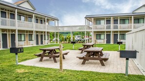A courtyard with picnic tables and mailboxes, surrounded by a building with balconies and a view of a parking area.
