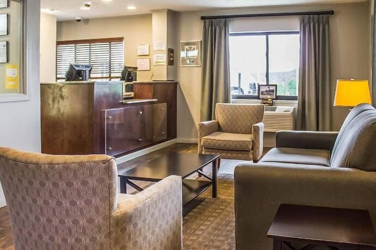 A hotel room with a reception desk, two armchairs, a sofa, a small table, and a window with curtains.