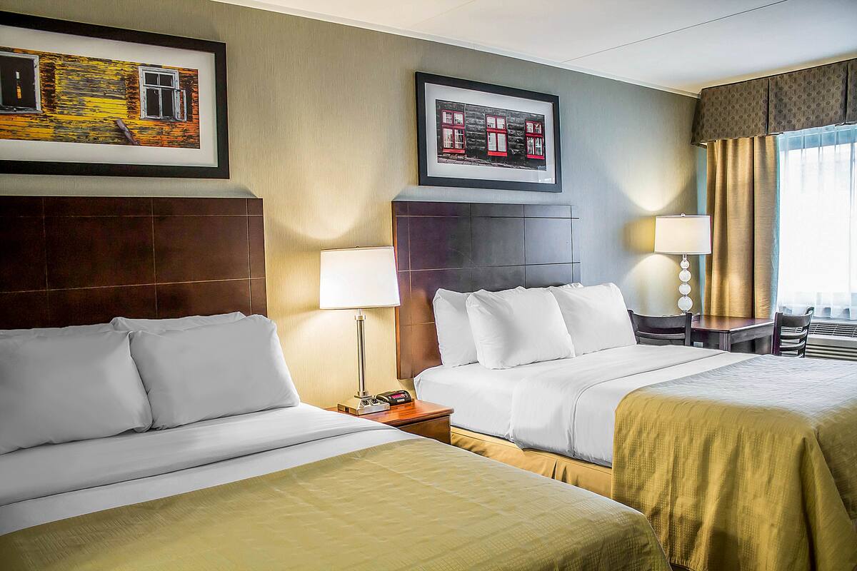 A hotel room with two beds, a nightstand, a lamp, and framed pictures on the wall.