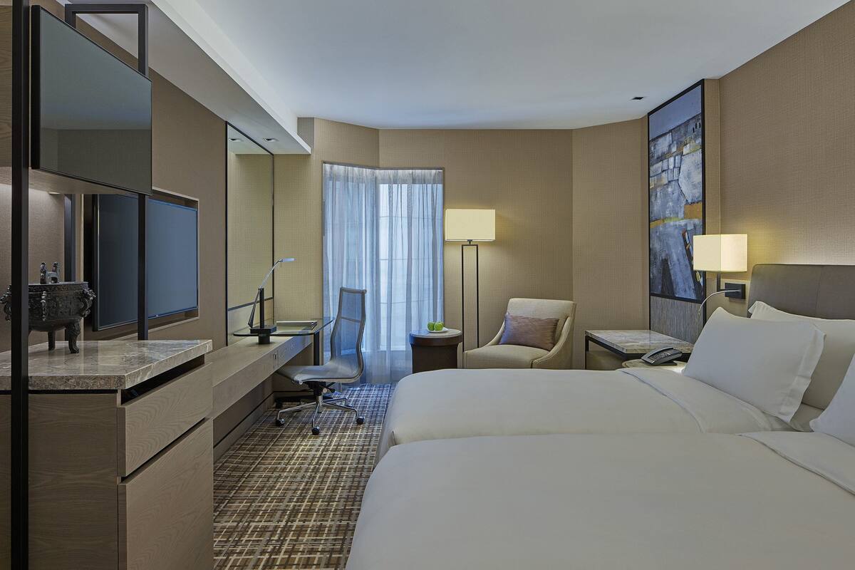 Une chambre d’hôtel avec un grand lit, un bureau doté d’un téléviseur à écran plat, une chaise, une petite table avec une lampe et un tableau au mur.