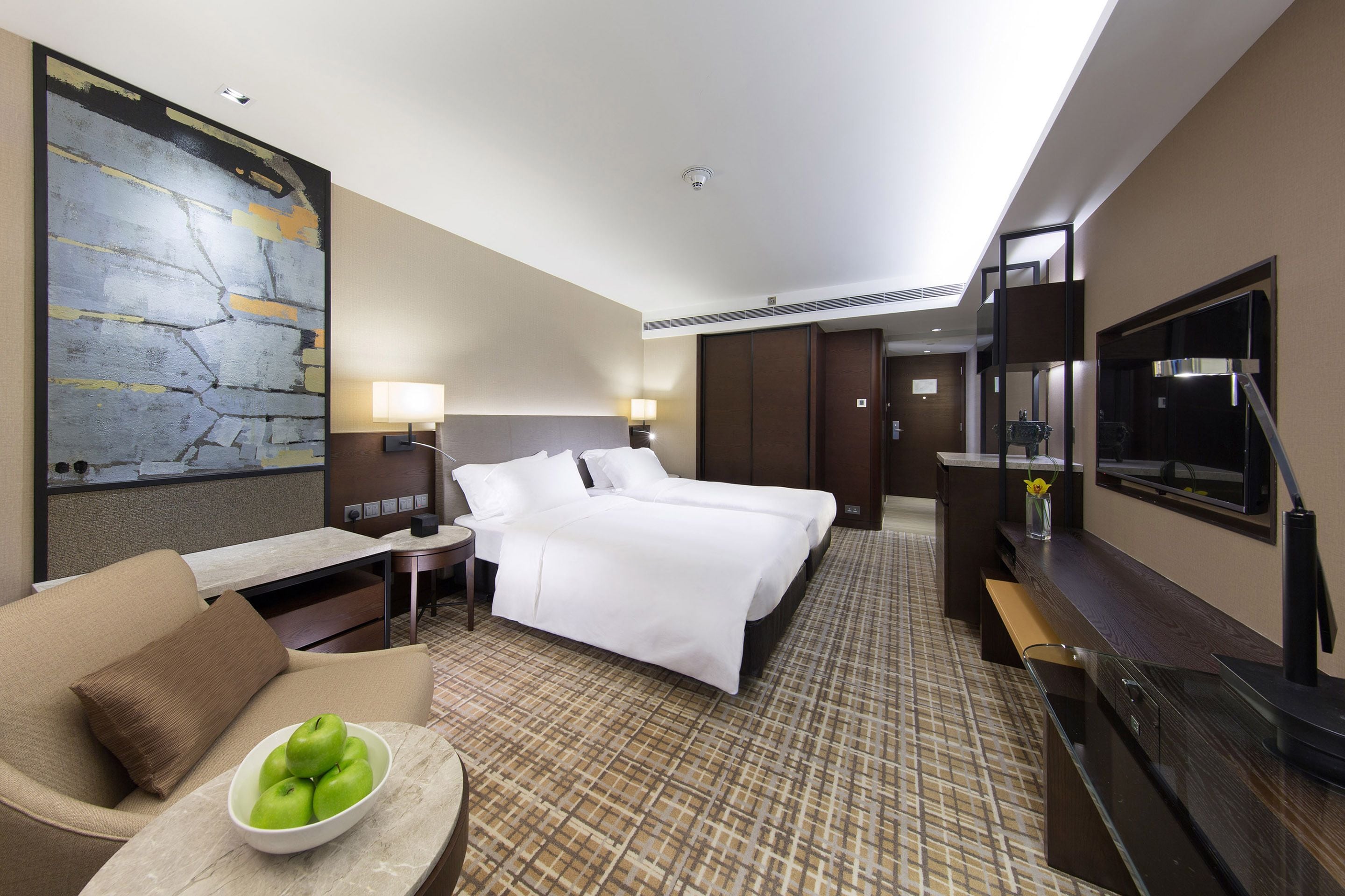 A hotel room with a large bed, a desk with a lamp, a TV, and a painting on the wall.