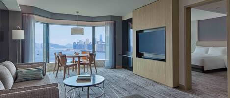 A modern hotel room with a city view, a dining area, a TV, and a bed.