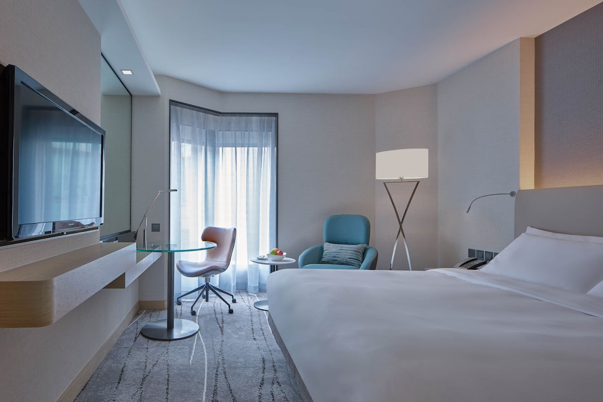 Une chambre d’hôtel équipée d’un lit, d’une télévision, d’un bureau avec une chaise, d’une lampe et d’une fenêtre avec des rideaux.