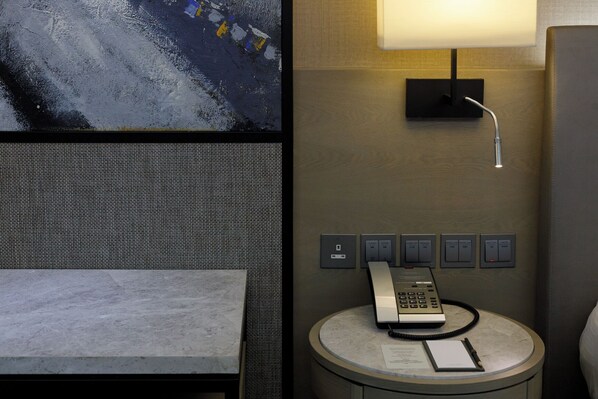 Habitación de hotel con cama, una mesa redonda, teléfono y bloc de notas, una lámpara de pared y un enchufe.