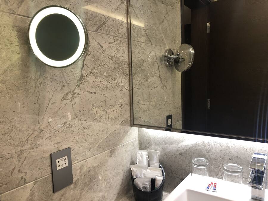 Un baño moderno con pared de mármol, un espejo redondo, ducha con puerta de vidrio y zona de lavamanos con artículos de aseo.