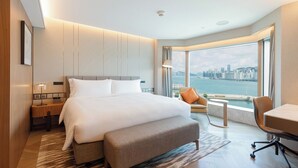 A modern hotel room with a large bed, a desk, and a view of a city skyline. - New World Millennium Hong Kong Hotel (Kowloon)