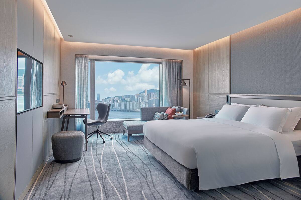 Une chambre d’hôtel moderne, dotée d’un grand lit, d’un bureau, d’une chaise et offrant une vue sur le paysage urbain.
