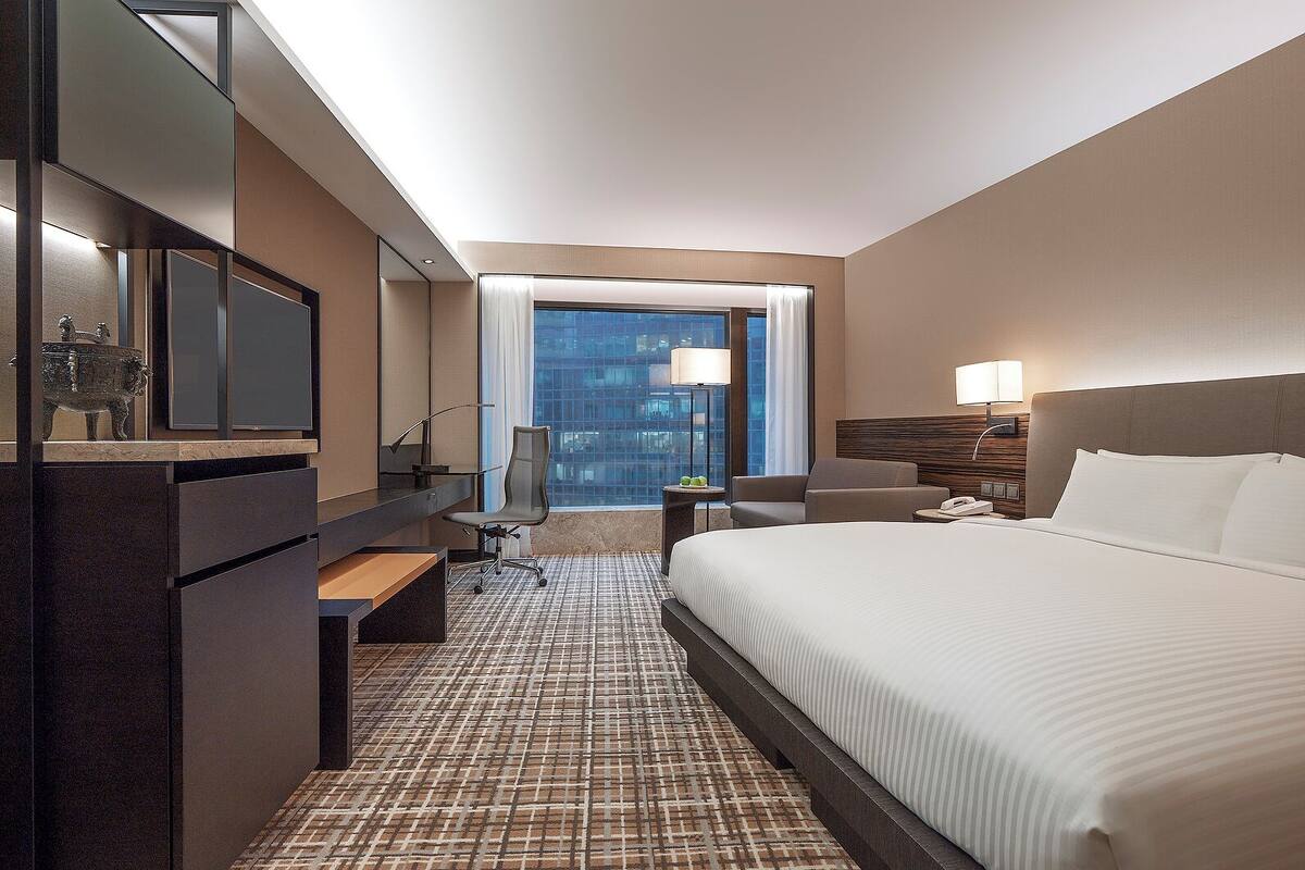Une chambre d’hôtel avec un grand lit, un bureau avec une chaise, une télévision, une lampe et une vue sur la ville.