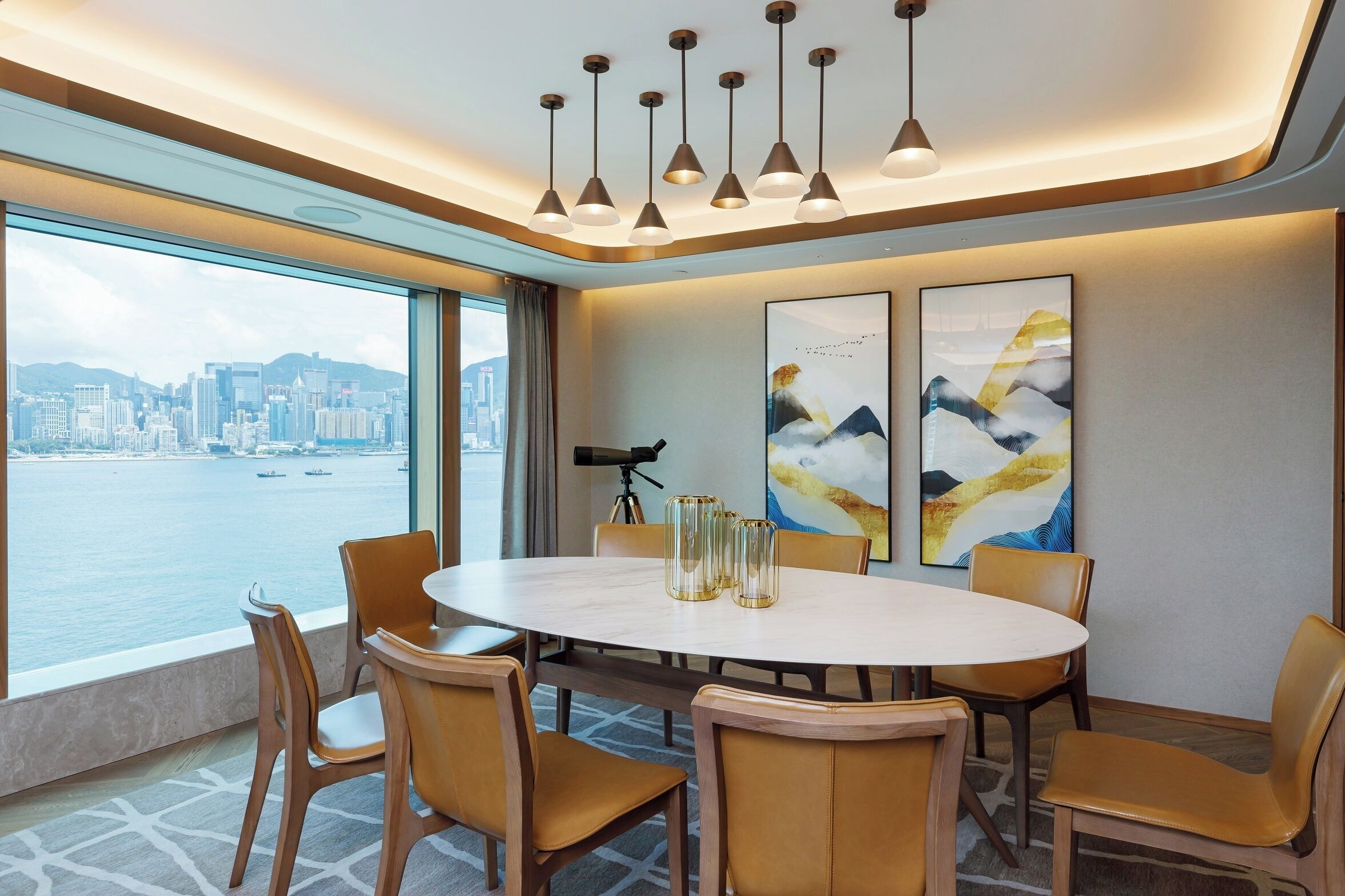 A modern dining area with a round table, chairs, and pendant lighting. A cityscape view is visible through large windows.