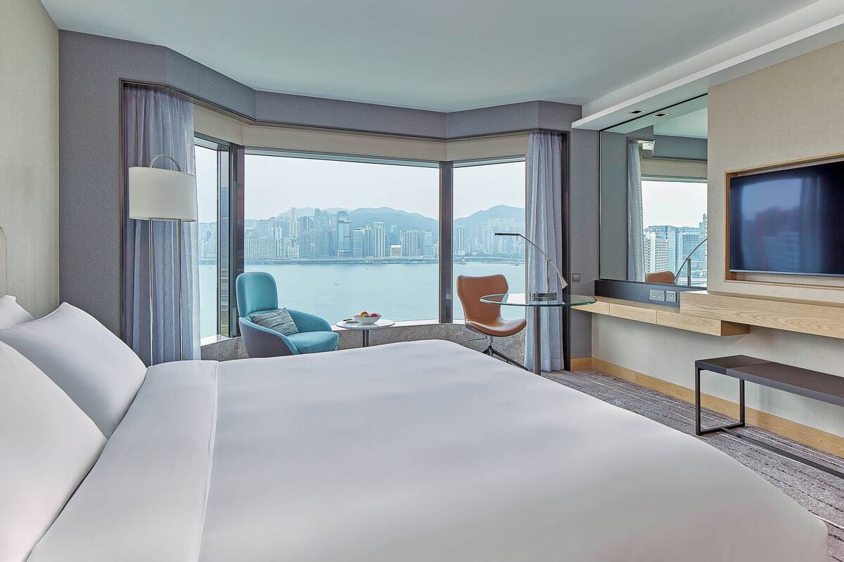 Une chambre d’hôtel avec un grand lit, un bureau avec une télévision, une chaise et une vue sur le paysage urbain.