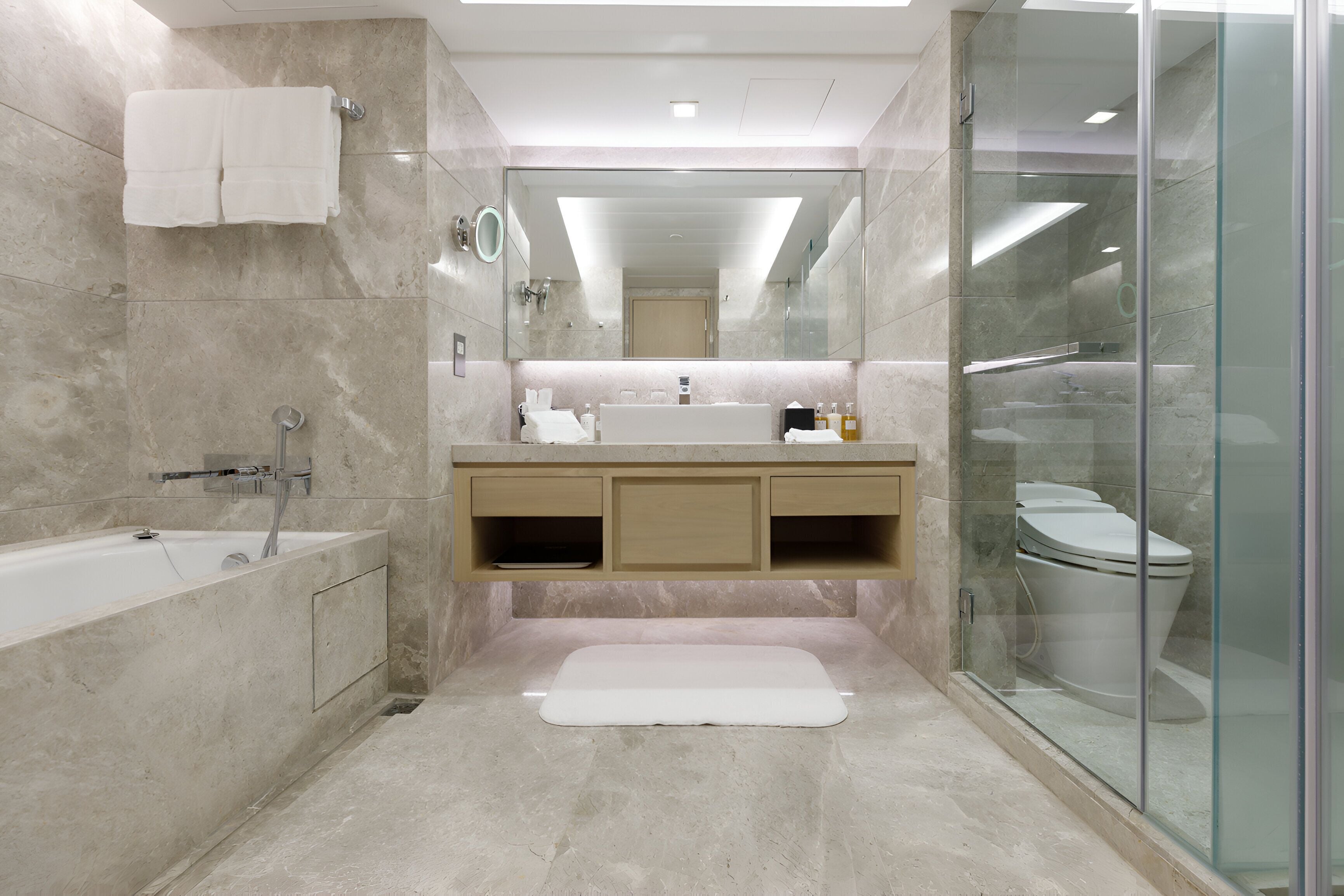 A modern bathroom with a bathtub, a glass-enclosed shower, a vanity with a sink, and a toilet.