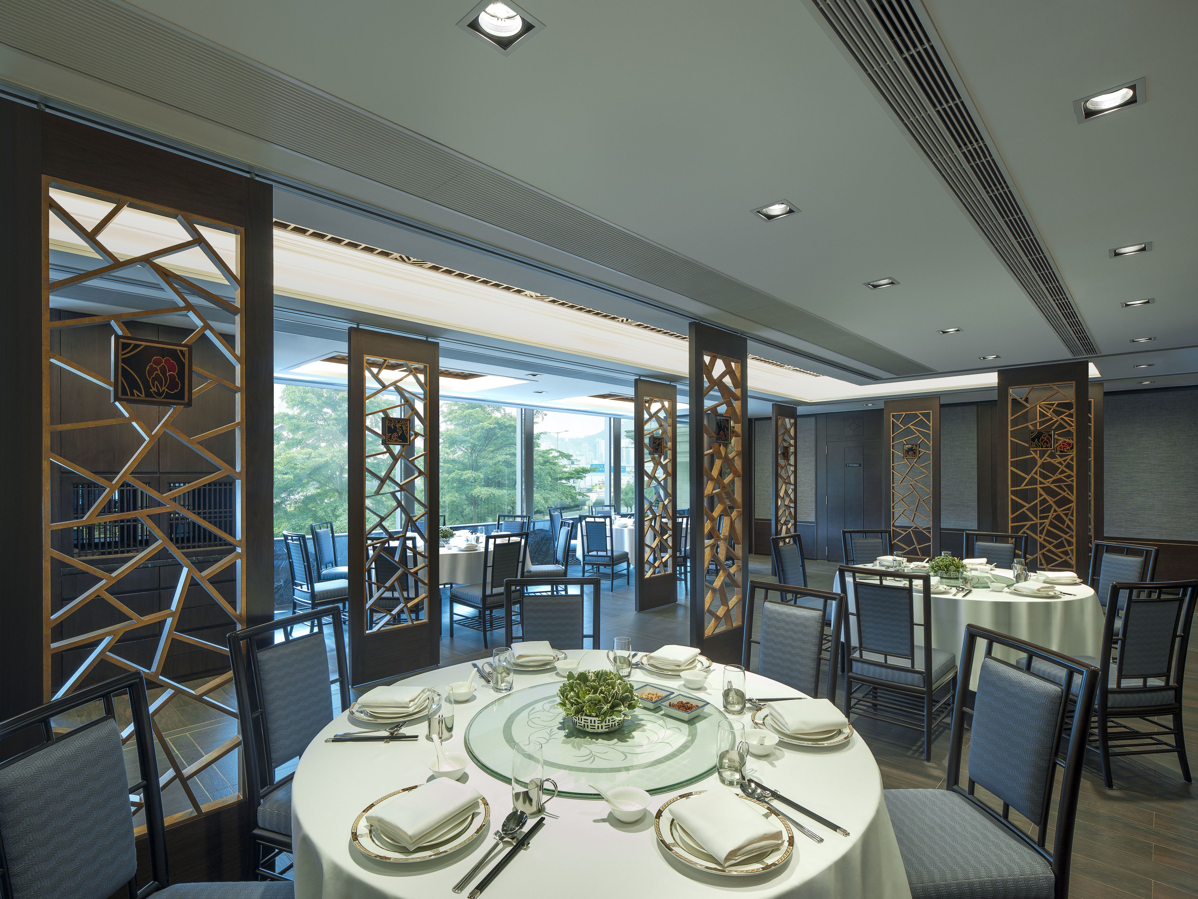 A dining area with round tables set for a meal, featuring a view of greenery outside.