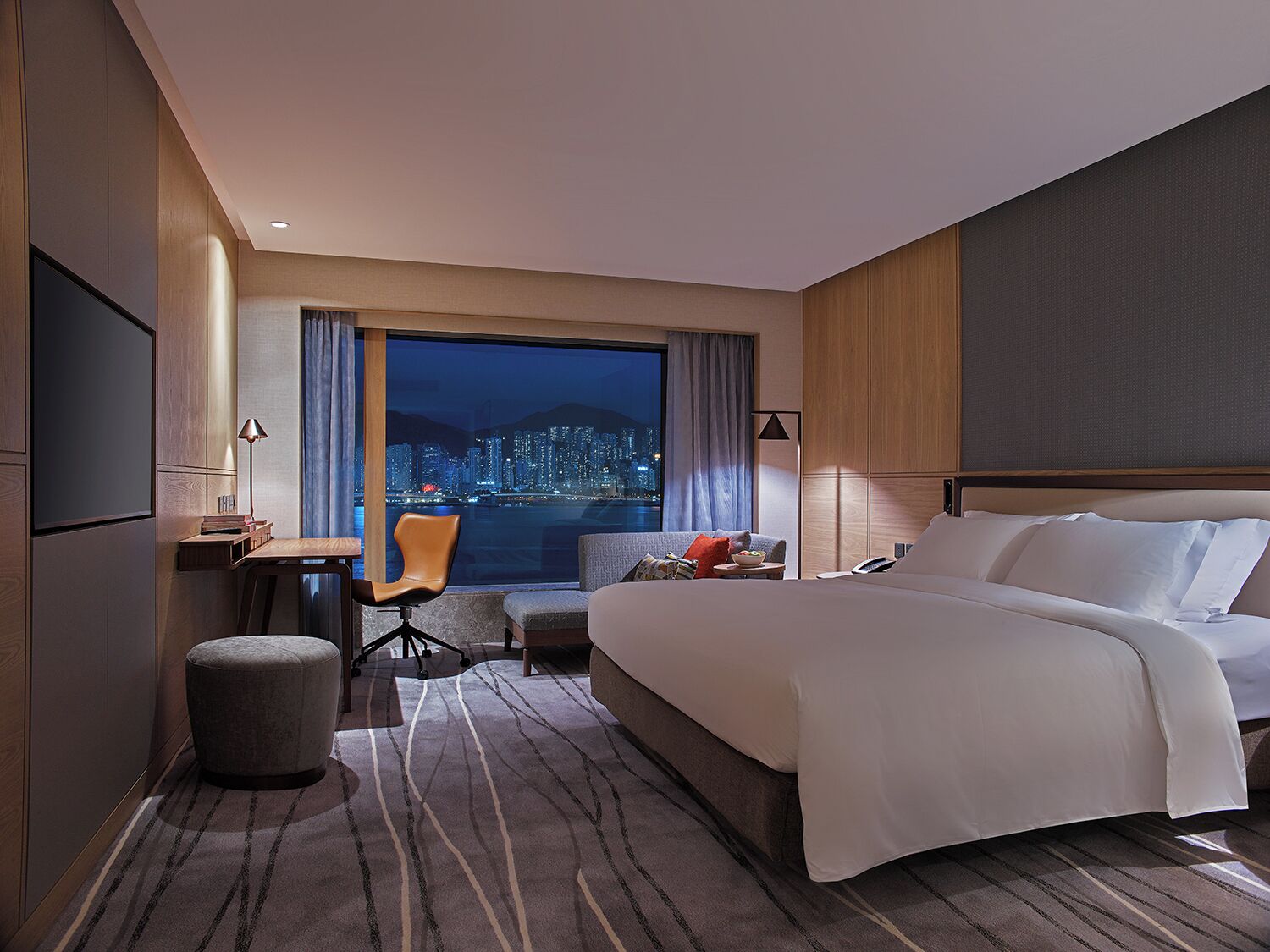 Habitación de hotel moderna con una cama grande, un escritorio, una silla y vistas a un paisaje urbano de noche.