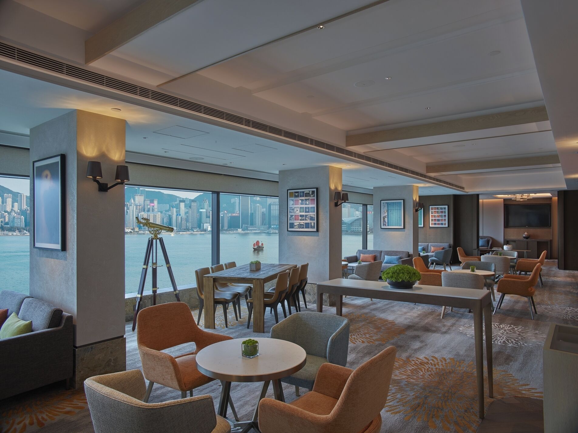 A modern hotel lobby with a large window offering a city view, a dining area, and a seating area with a view of the water.