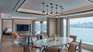 Ett modernt hotellrum med ett stort matbord, bekväma sittplatser, en platt-TV och utsikt över staden.