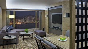A modern hotel room with a city view, a sofa, a dining table with apples, and a TV. - New World Millennium Hong Kong Hotel (Kowloon)