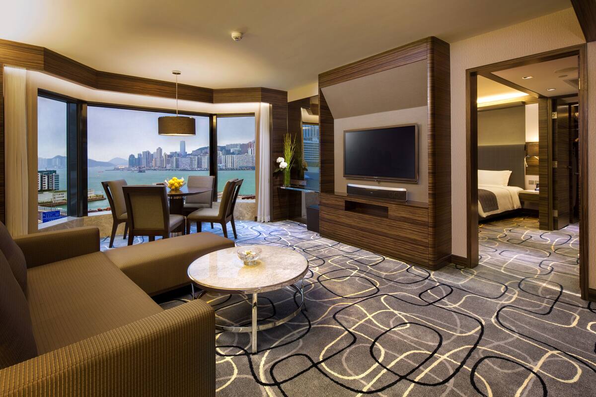 Une chambre d’hôtel moderne dotée d’une grande télévision, de sièges confortables, d’un coin repas et offrant une vue sur la ville.