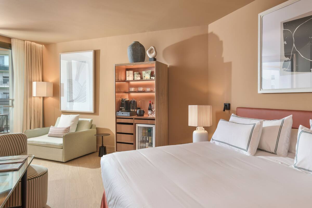 A hotel room with a large bed, a sofa, a coffee table, a bookshelf, and a desk.