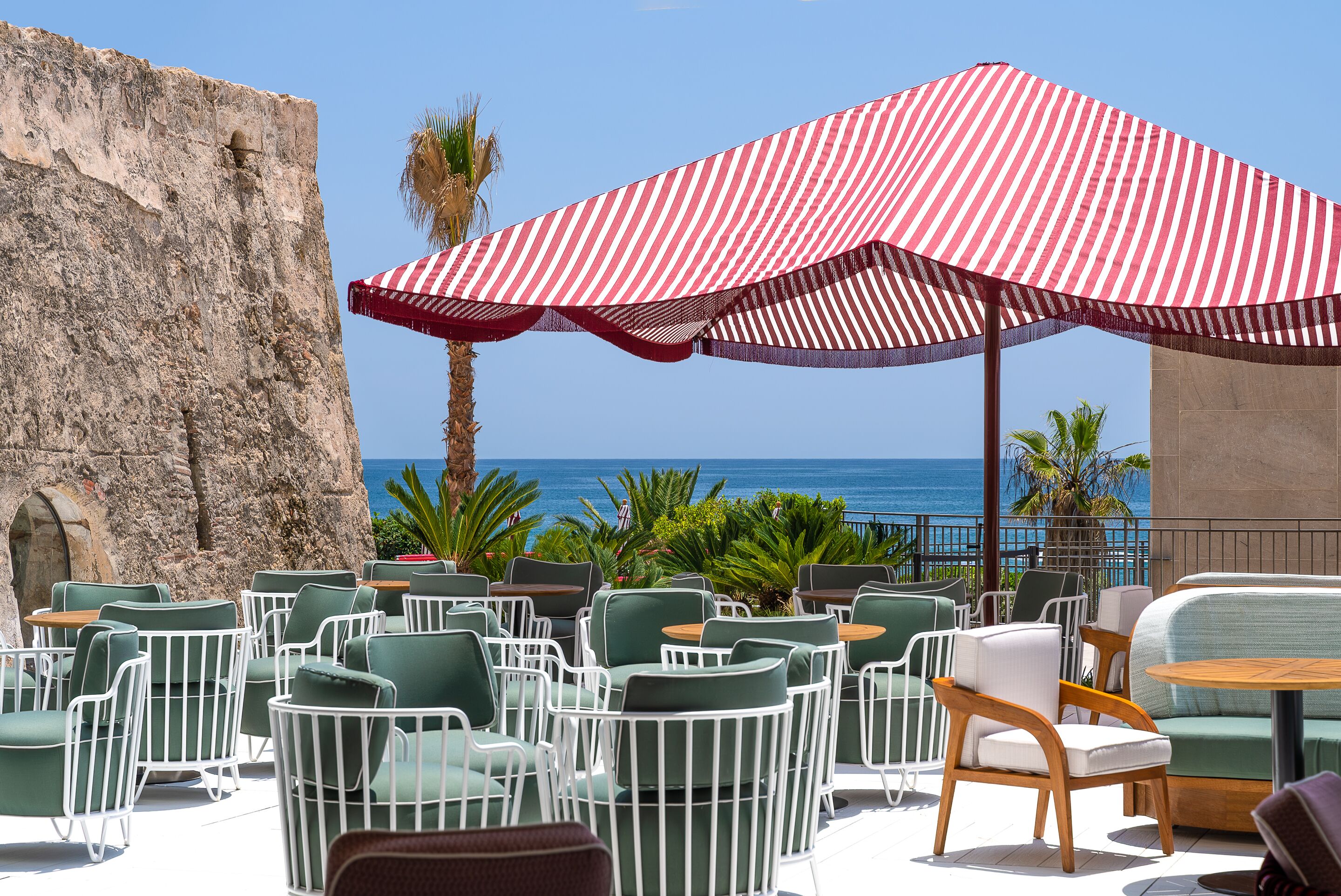 Outdoor seating with a view of the ocean, a red and white striped umbrella, and a stone wall.
