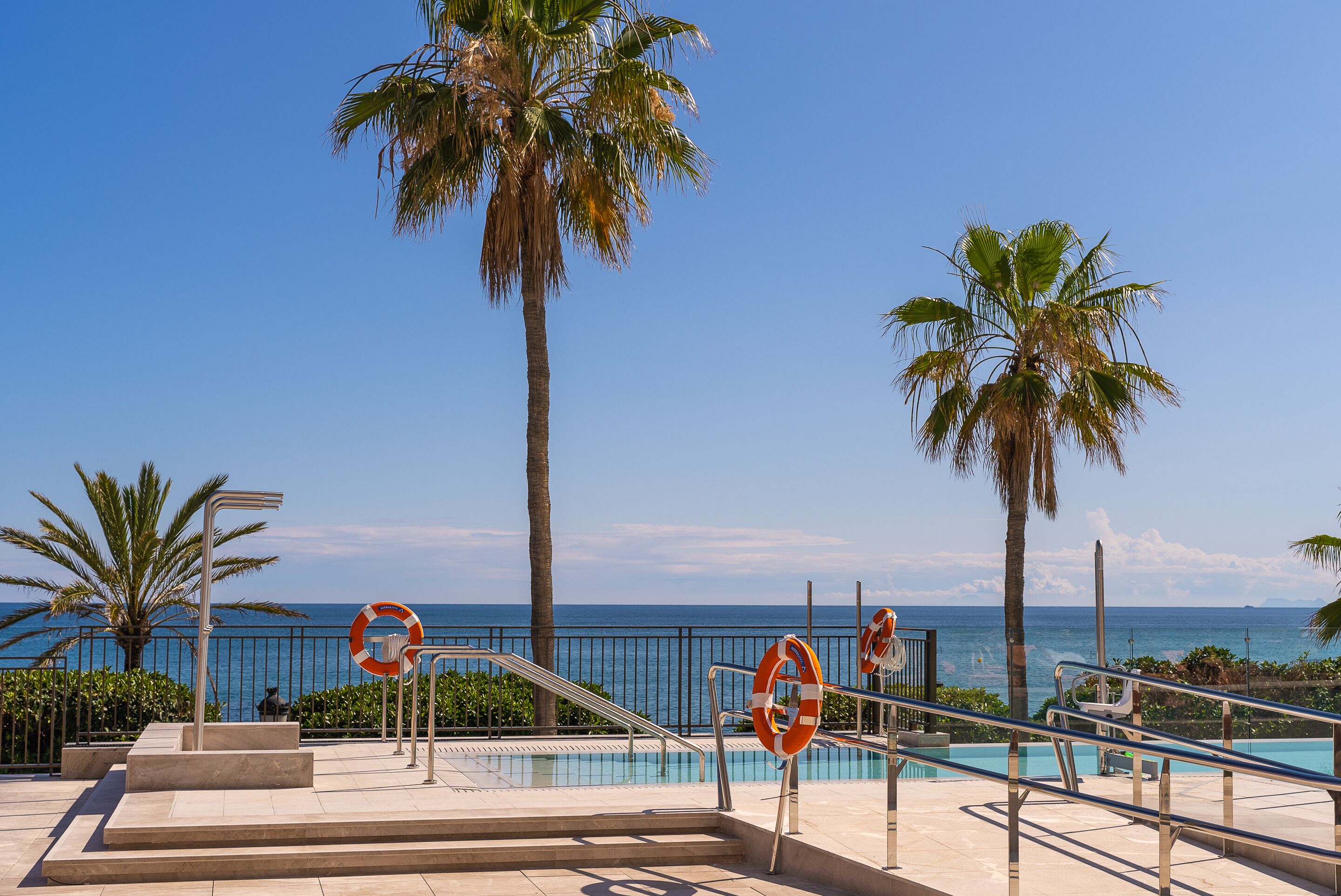 Zona de piscina amb boies, palmeres i vista a l'oceà.