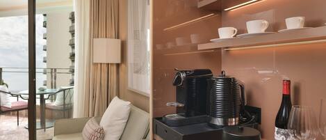 Une chambre d’hôtel moderne avec un canapé, une machine à café, une bouteille de vin et des tasses sur une étagère.
