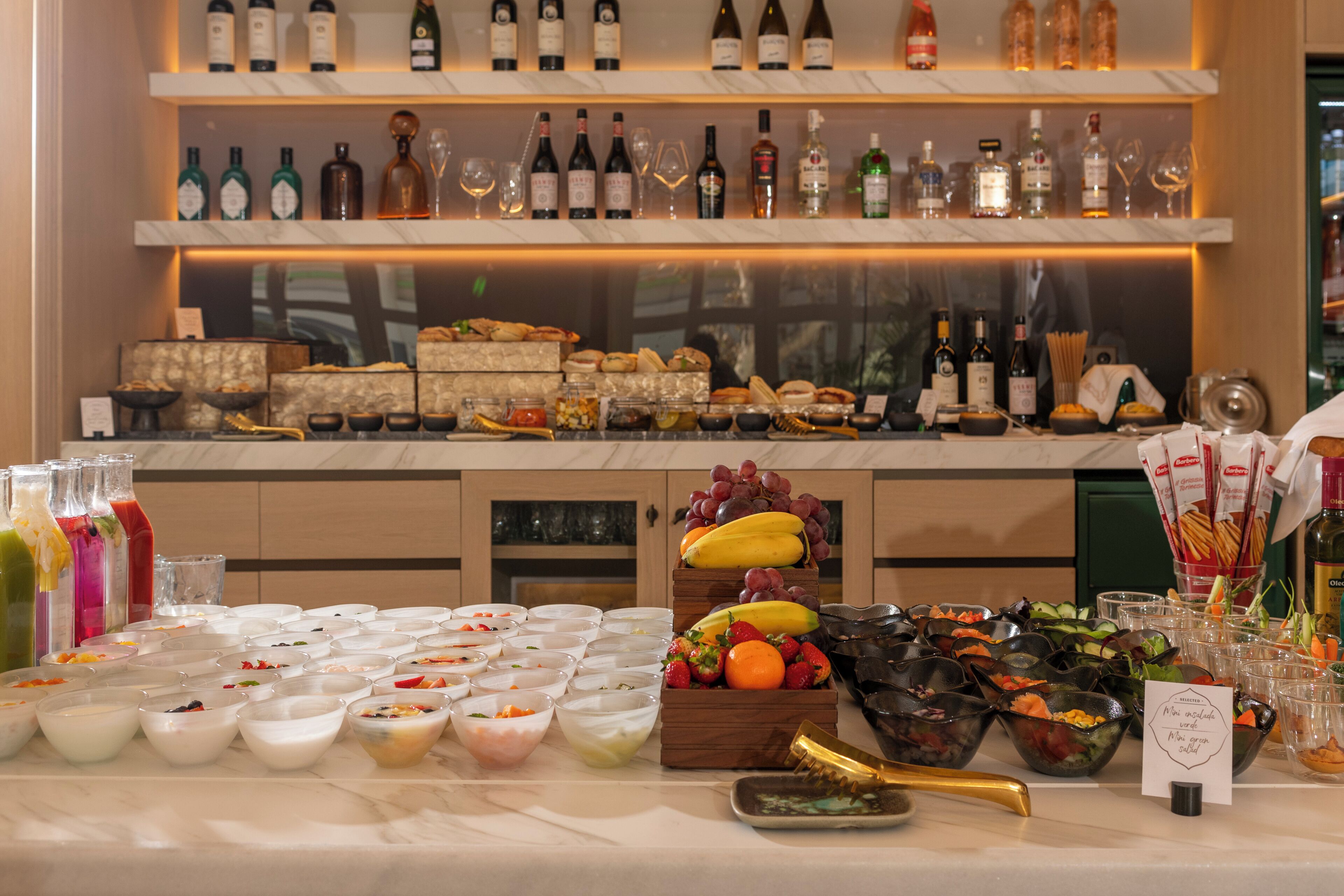 A buffet with various food items and a selection of wine bottles on shelves.