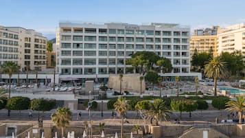 Un hotel con varios pisos, zona de piscina al aire libre y palmeras.