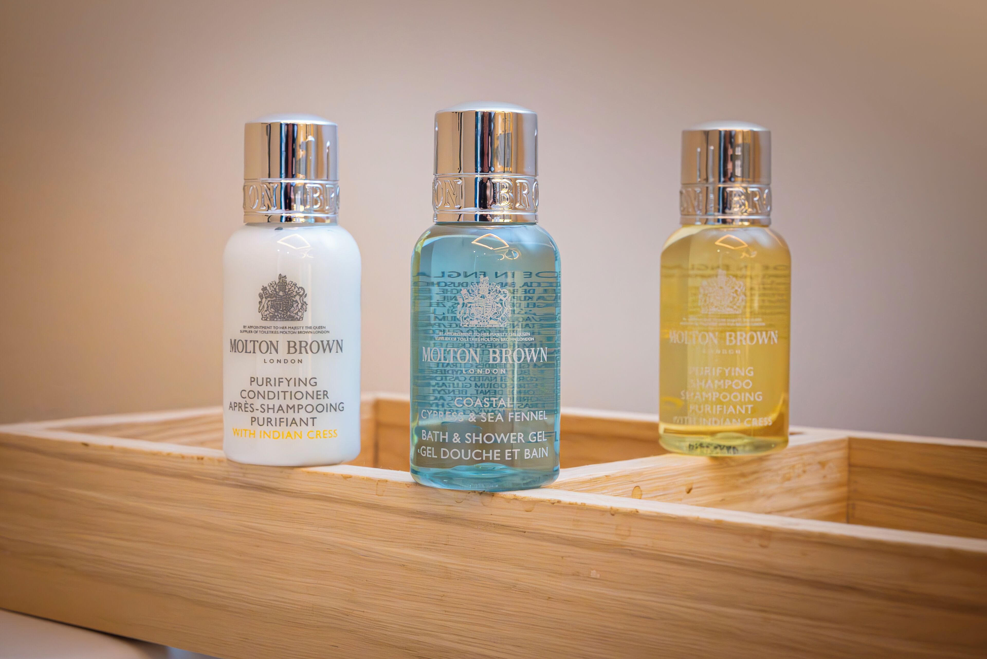 Three bottles of Molton Brown toiletries in a wooden tray.