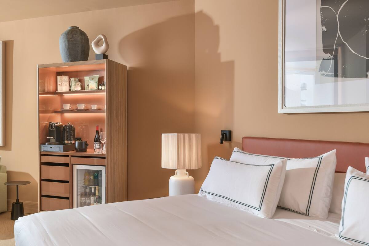 A hotel room with a large bed, a minibar, a seating area, and a wall-mounted artwork.