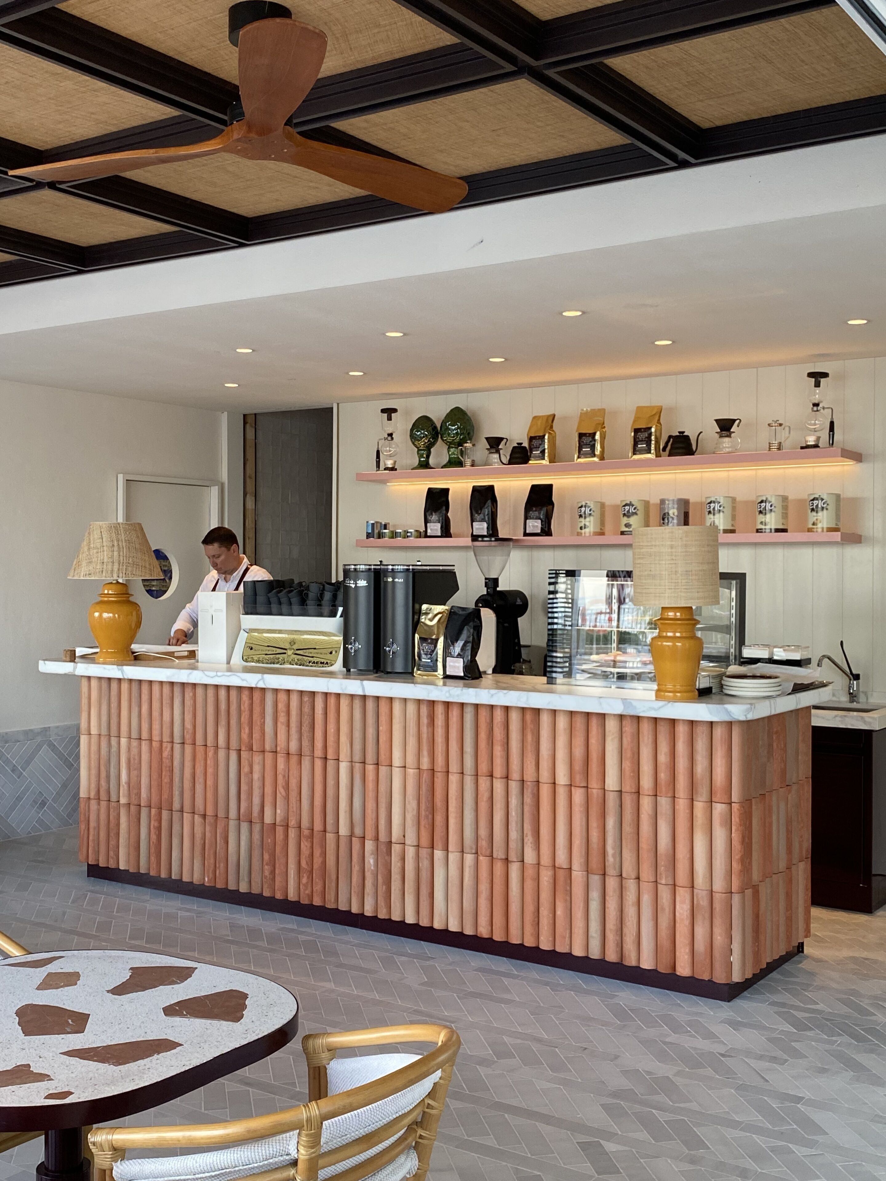 Zona de bar moderna con una isla central, mostrador de listones de madera y un ventilador de techo.