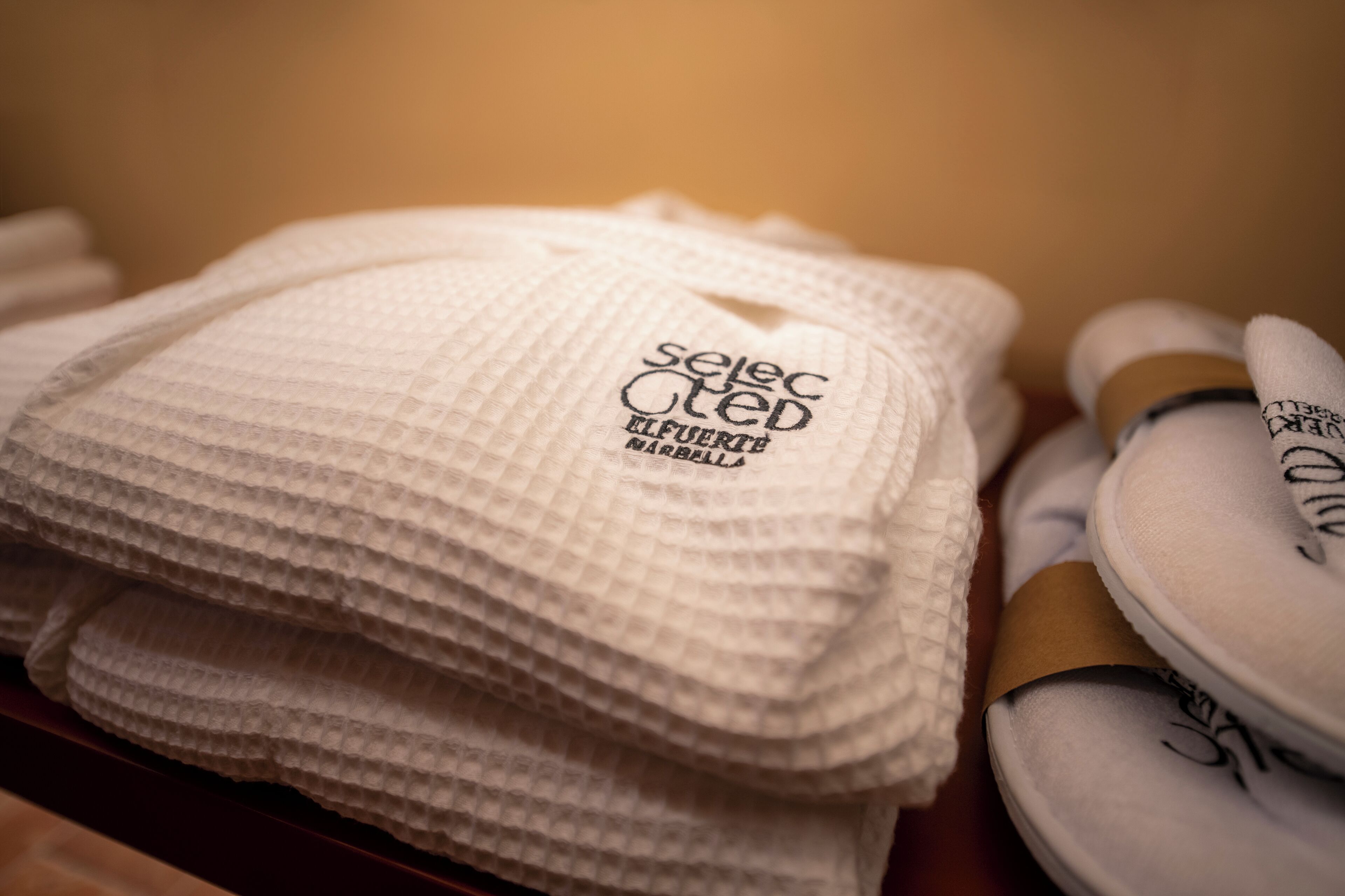 Une pile de serviettes blanches ornées de motifs brodés et une paire de baskets blanches avec des inscriptions noires.