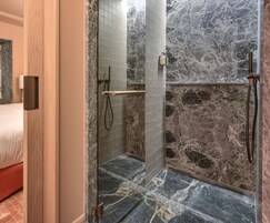 Een douche met een marmeren wand en een houten deur.