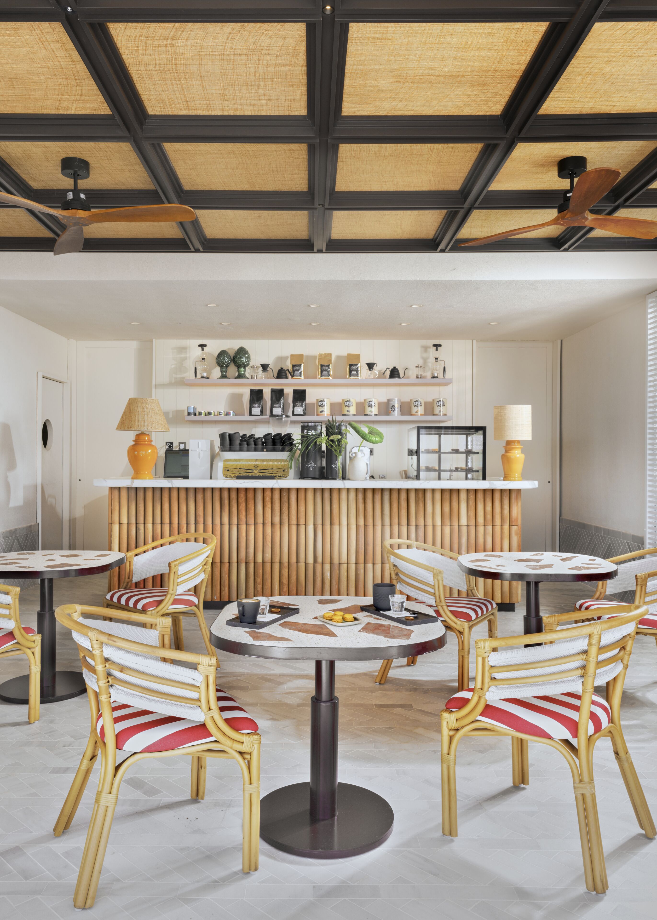 A modern cafe with round tables and wicker chairs, a bamboo wall, and a variety of items on shelves.
