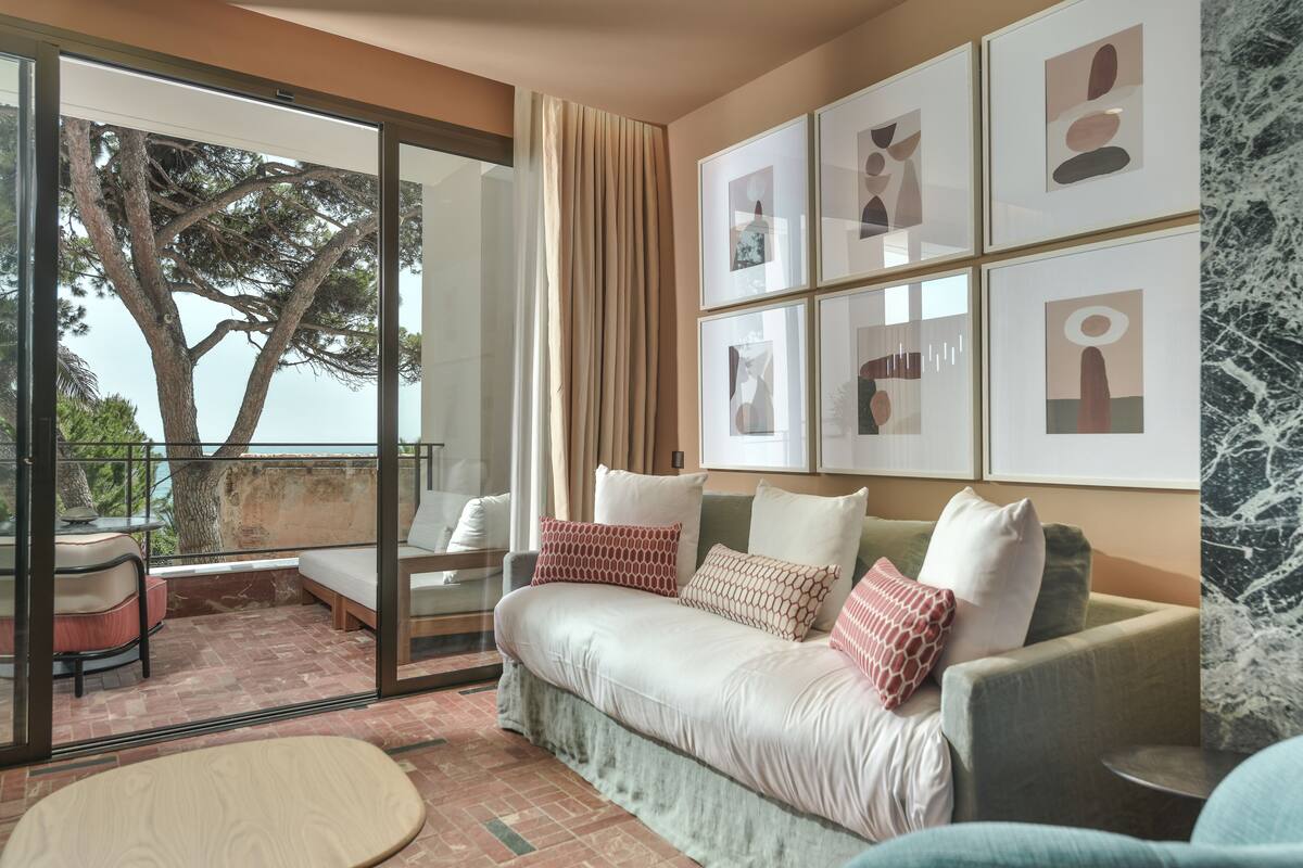 A modern living room with a sofa, a coffee table, and a balcony with a view of trees.