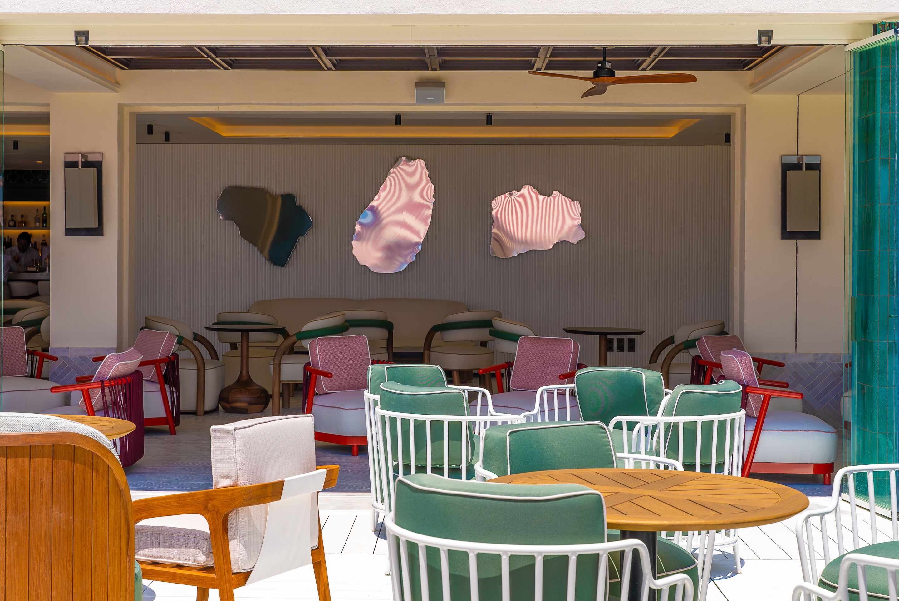 Un espace extérieur moderne, aménagé avec des chaises vertes et blanches, une table en bois et des œuvres d’art abstraites murales.