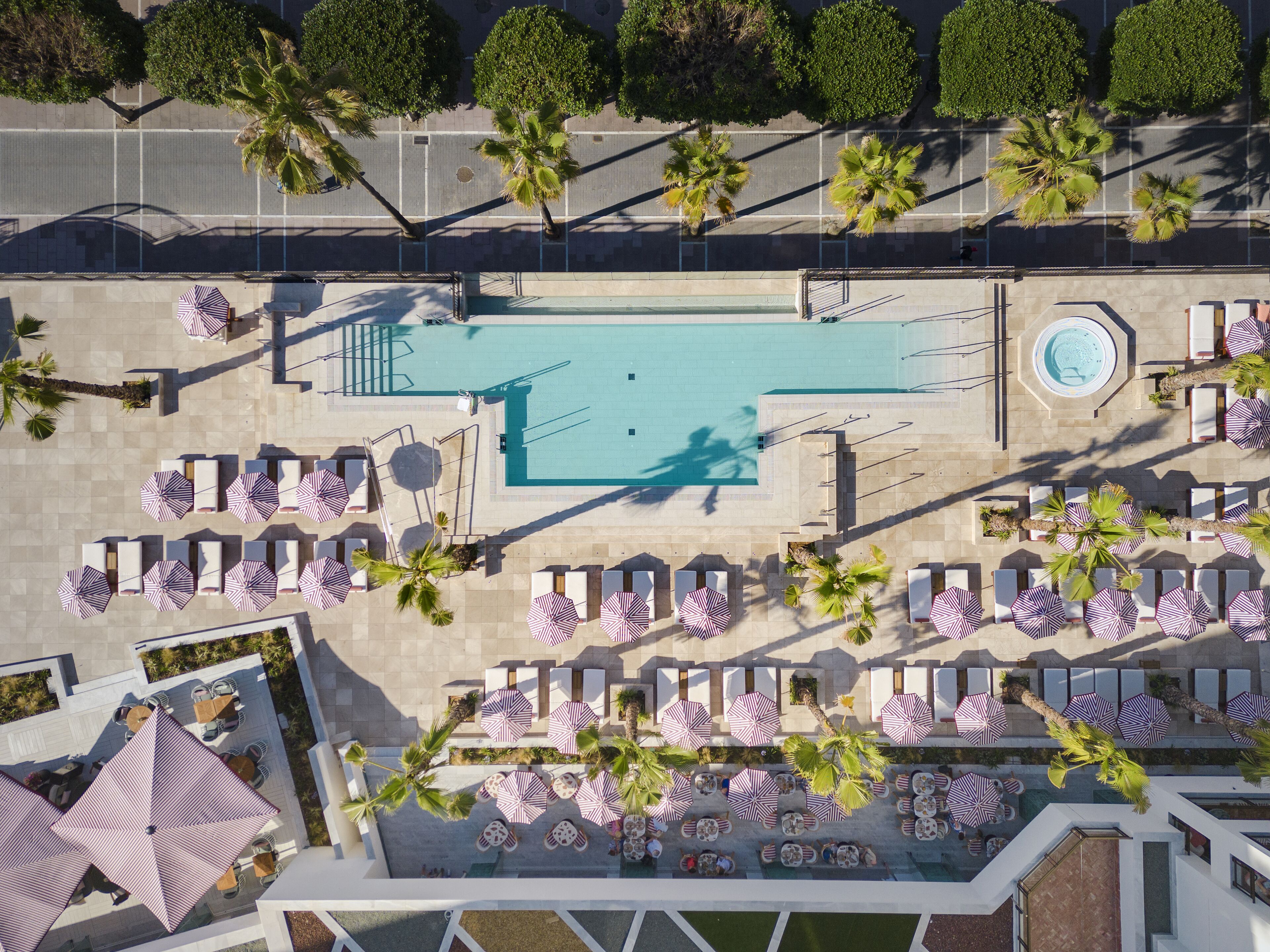 Luchtbeeld van een resort met een zwembad, ligbedden, parasols en palmbomen.