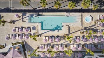 Luchtbeeld van een resort met een zwembad, ligbedden, parasols en palmbomen.