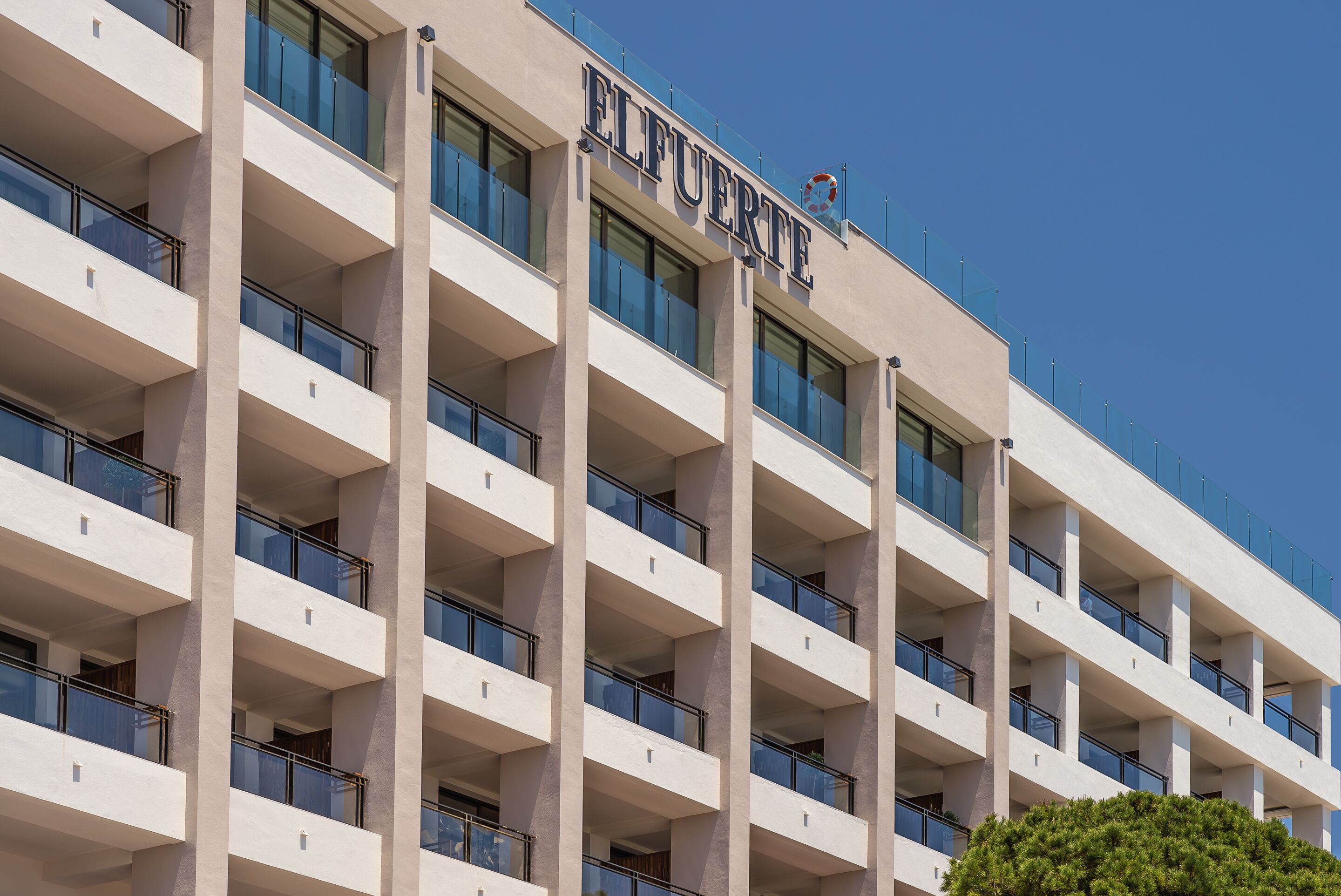 Un edificio de varios pisos con el nombre "EL FUERTE" bien visible. Presenta un estilo arquitectónico moderno con una serie de balcones y grandes ventanales.