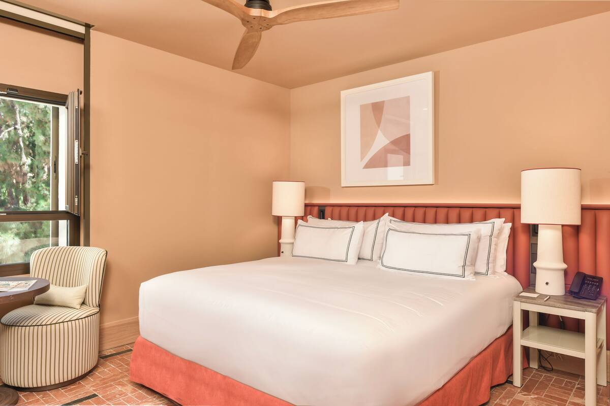 A hotel room with a large bed, two bedside lamps, a chair, a small table, and a ceiling fan.