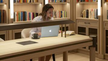 A person using a laptop at a table in a library with bookshelves in the background.