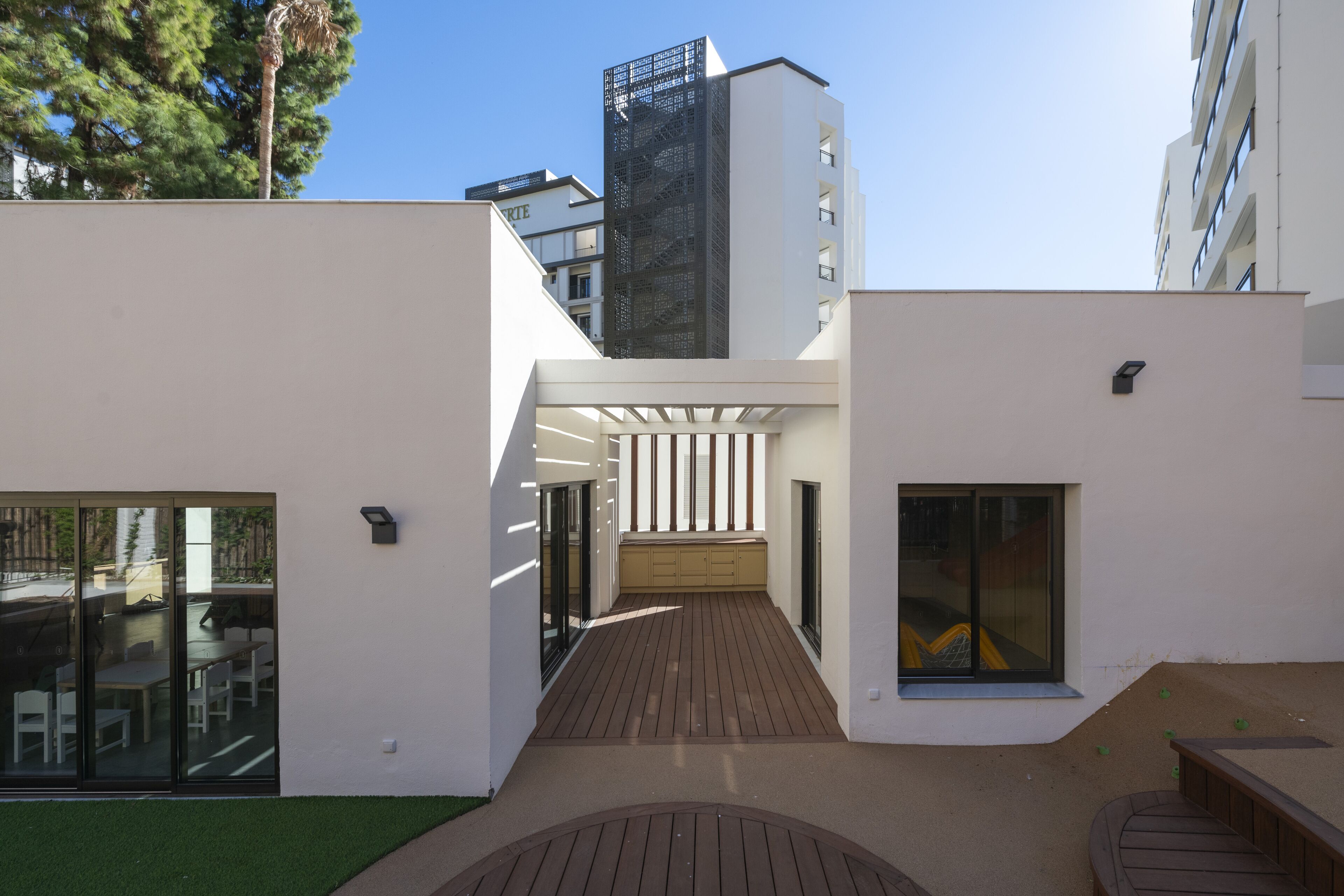 Een modern gebouw met een houten terras, grote ramen en een heldere lucht.