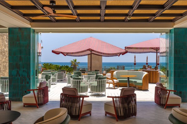 A terrace with outdoor seating, a view of the ocean, and a ceiling fan.