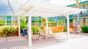 A covered outdoor area with lounge chairs and a pool, surrounded by greenery and a building with balconies. - GLH Hotel (Tucson)