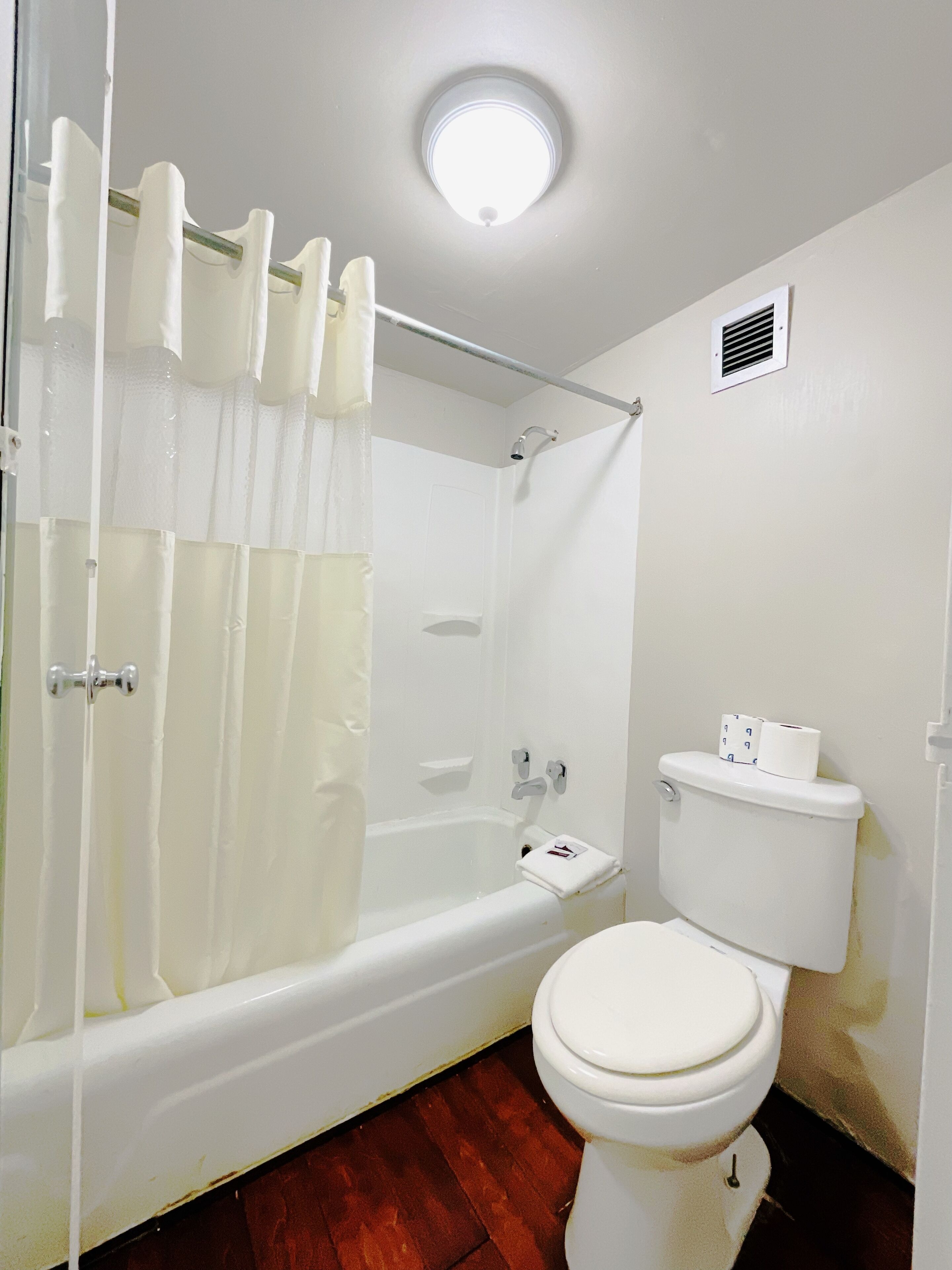 Un baño con bañera, cortina de ducha, inodoro y una lámpara en el techo.